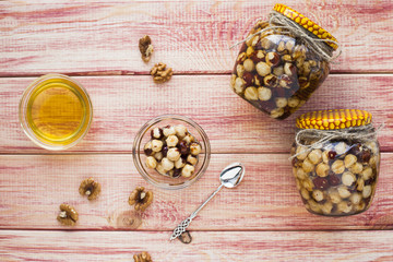 Natural honey and nuts in glass jars, vintage silver spoon on the wooden background. Healthy food, diet, lifestyle concept. Top view. Close up.