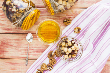 Natural honey and nuts in glass jars, vintage silver spoon on the wooden background. Healthy food, diet, lifestyle concept. Top view. Close up.