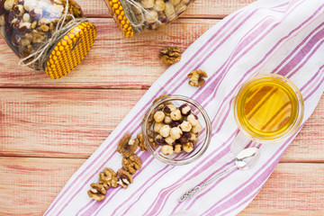 Natural honey and nuts in glass jars, vintage silver spoon on the wooden background. Healthy food, diet, lifestyle concept. Top view. Close up.