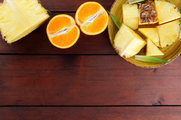 Pieces of pineapple and oranges on a yellow plate on wooden boards, pineapple and halves of orange...