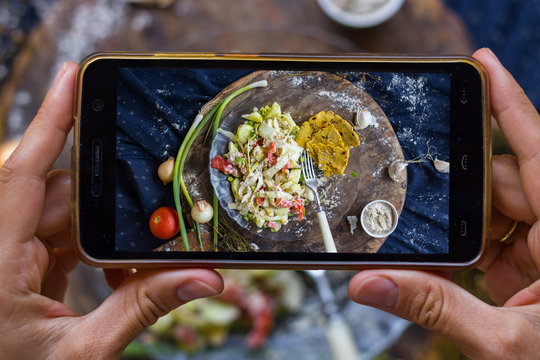 Woman hands take smartphone food photo of raw vegan zucchini spaghetti. Phone food photography for social media or blogging in popular and trendy top view style. Raw vegan vegetarian meal concept.