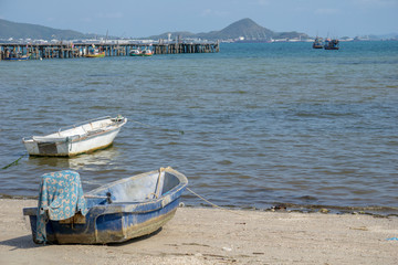 Small white and blue old fiberglass boats mooring at the beach in front of old wooden jetty in Thailand on the sunny day.