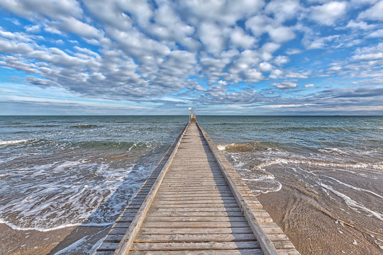 Ein Steg f&uuml;hrt ins Mittelmeer am Strand von Lido di Jesolo, Italien, mit einem prachtvollen Wolkenhimmel und sch&ouml;nen blau-t&uuml;rkisen Farben