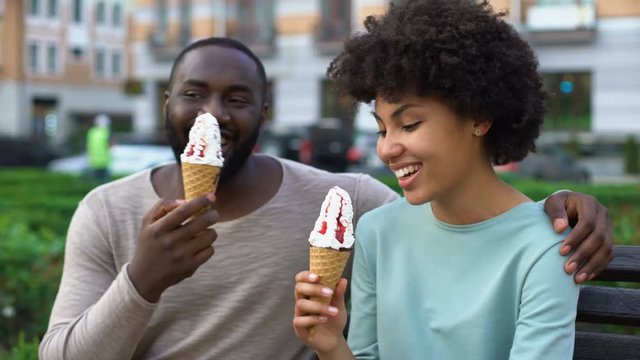 Dating couple eating ice-cream, sitting on city bench, having fun together, love