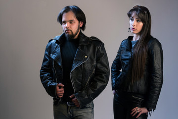 A couple of young people in black leather jackets. A guy and a girl in rocker or biker style posing in the studio.