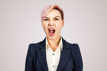 Young girl office worker with a screaming grimace looks at camera, isolated on a pink background