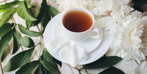 White porcelain cup of green tea and white fresh peonies on light gray wooden background. Top view, concept of relaxation.