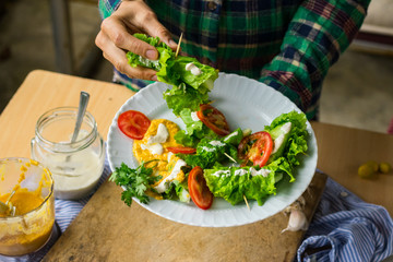 Woman hands holds vegan spring rolls. Cucumbers wrapped in salad leaves with tomatoes, vegan mustard sauce and homemade sesame seeds tahini paste. Vegetarian healthy food.