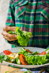 Woman hands holds vegan spring rolls. Cucumbers wrapped in salad leaves with tomatoes, vegan mustard sauce and homemade sesame seeds tahini paste. Vegetarian healthy food.