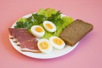 breakfast. Boiled eggs, bacon, greens in a white plate on pink background