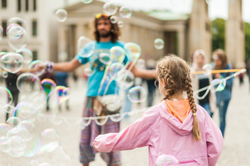 Street performer, busker, entertaining the crowd in front of the Brandenburg Gate in Berlin on an overcast summer day. Children playing with colorful soap bubbles floating in the foreground.