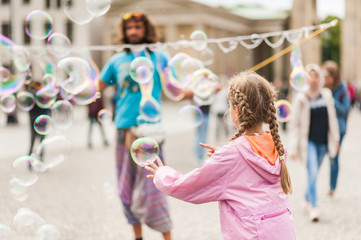 Street performer, busker, entertaining the crowd in front of the Brandenburg Gate in Berlin on an overcast summer day. Children playing with colorful soap bubbles floating in the foreground.