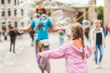 Fototapeta premium Street performer, busker, entertaining the crowd in front of the Brandenburg Gate in Berlin on an overcast summer day. Children playing with colorful soap bubbles floating in the foreground.