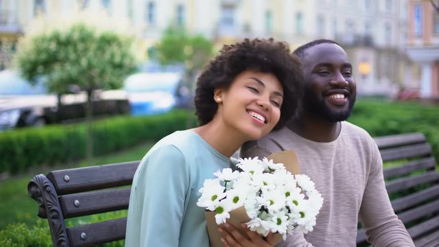 Beautiful african girl feeling happy with flowers on date, sweet couple hugging