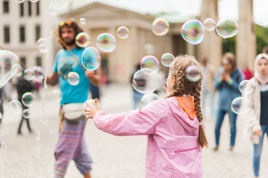 Street performer, busker, entertaining the crowd in front of the Brandenburg Gate in Berlin on an overcast summer day. Children playing with colorful soap bubbles floating in the foreground.