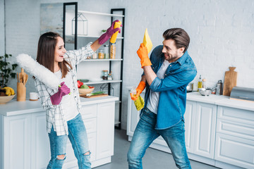 couple having fun during cleaning kitchen and fighting with cleaning tools