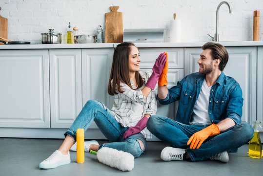 couple sitting on floor and giving high five after cleaning in kitchen