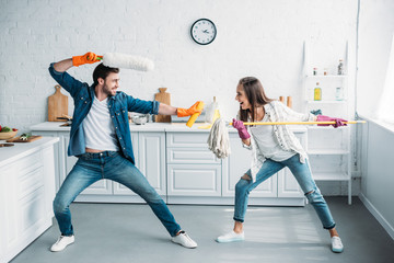 couple having fun and pretending fight with cleaning tools in kitchen