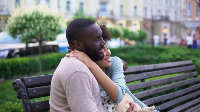 Afro-american loving couple nuzzling on bench, enjoying summer day together
