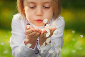 Closeup portrait girl blowing flower petals in the park on a summer day