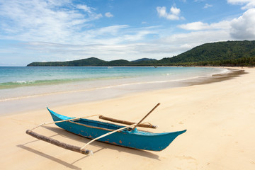 Traditional fishing boat on shore of the ocean with white sand