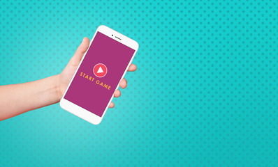 Kid hand holding smartphone with start game text on screen on blue background.