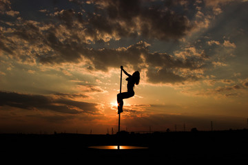 Pole dancer girl perfoms a trick on a pilon on sunset sky