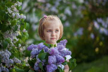 Clooseup cute portrait little girl with a bouquet of lilacs in spring