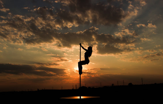 Contrast silhouette photos at sunset against the sky: girl poledancer performs an element on the pole with the bend in the back