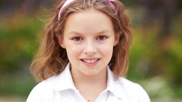 Close up of a little blonde brown-eyed cute girl face. Girl blinking her eyes and smiling. Inside. Portrait shot. Happy schoolgirl
