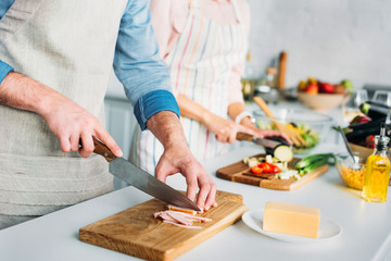 cropped image of couple cooking and cutting vegetables with meat in kitchen