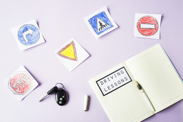 Training notebook for driving lessons and driving traffic rules next to the road sign drawings to get a driving license. On a purple background next to the car keys