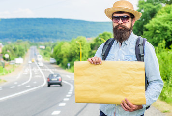 Man bearded hitchhiker stand at edge of road with blank paper sign, copy space. Benefits using sign with name destination. Cardboard sign with indication where you want go. Short general directions