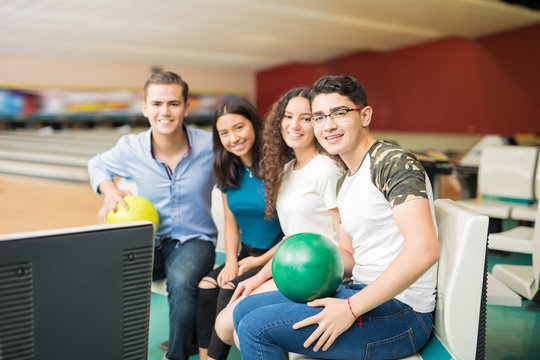Confident Friends With Bowling Balls Sitting In Club