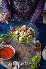 Woman hands holds fresh salad with raw cauliflower, red bell pepper, cucumber and dressed with white sesame seeds. Raw vegan vegetarian healthy food