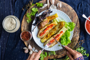 Woman hands cut roasted  grilled eggplants with fork and knife dressed with tomato garlic sauce, paprika, pepper and fresh salad leaves for lunch or dinner. Raw vegan vegetarian healthy food.