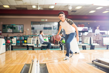 Teen Boy Throwing Ball While Practicing Bowling Game In Club