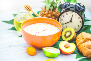 morning breakfast, muesli, fruit, peaches, honey and pineapple on a light background with green leaves Awakening with an alarm clock Healthy breakfast freshness Closeup