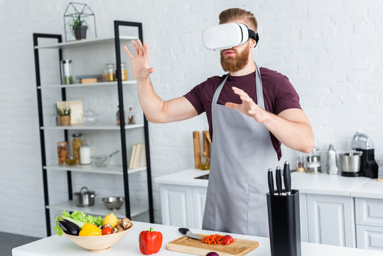 young man in apron using virtual reality headset while cooking in kitchen