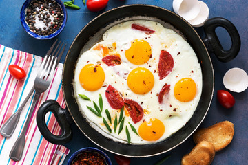 Fried eggs with tomatoes served in a pan with toast on a blue background. Flat lay