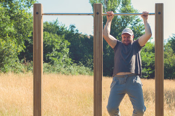Young man with excess weight doing pull up exercise on horizontal bar