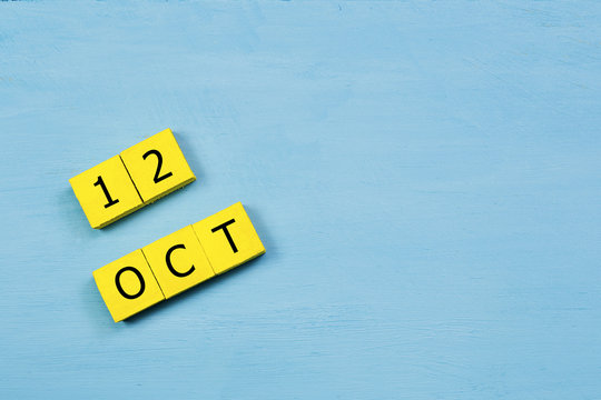 OCT 12, yellow cube calendar on blue wooden surface with copy space