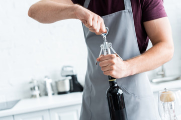 cropped shot of man in apron opening bottle of wine
