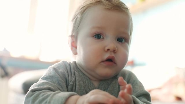portrait of blonde caucasian baby boy 10 months old standing at home thoughtful looking at camera and putting hands up sad upset face asking to pick up lovely cute healthy child happy motherhood