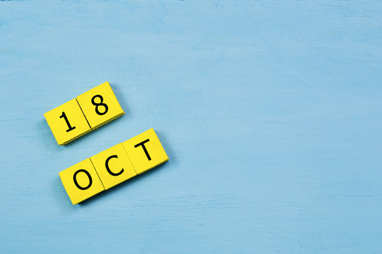 OCT 18, yellow cube calendar on blue wooden surface with copy space