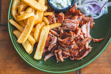 Gyros, Döner vom Spieß mit Kartoffel Pommes Frites, Zaziki und roten Zwiebel auf einem Teller in einem Restaurant serviert.