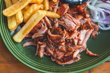 Gyros, Döner vom Spieß mit Kartoffel Pommes Frites, Zaziki und roten Zwiebel auf einem Teller in einem Restaurant serviert.
