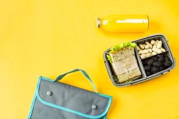 Foto op Canvas Lunchbox met eten - een broodje, noten en bessen - naast een fles sinaasappelsap en een tas voor een lunch. Eten dat je mee kunt nemen. Bovenaanzicht, plat gelegd, © svitlini