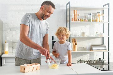 father and son whisking eggs in bowl on tabletop at kitchen