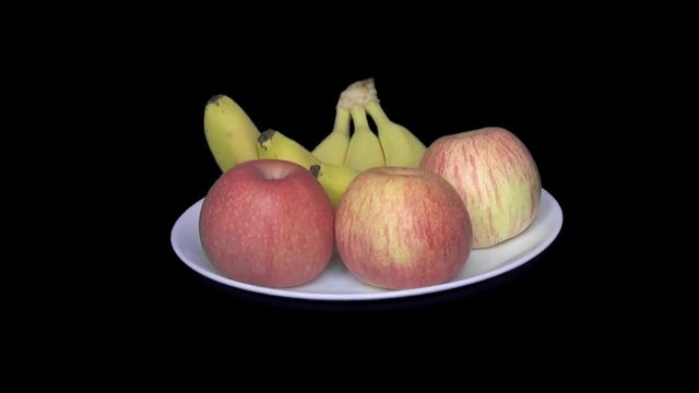 Three apples and three bananas lie on a white plate rotating horizontally 360 degrees